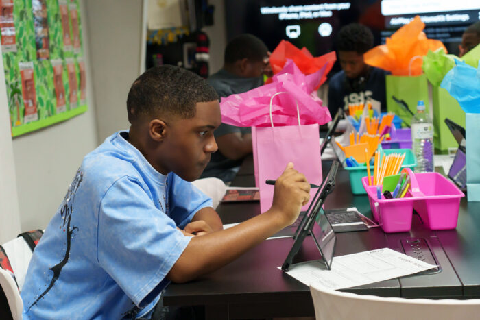 A student uses a stylus on a laptop at a table.
