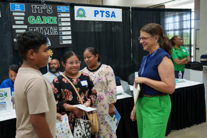 A family liaison talks with a smiling family at open house.