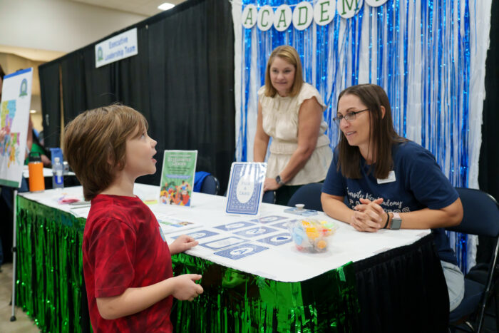 A student talks to smiling staff members at a brightly decorated table.