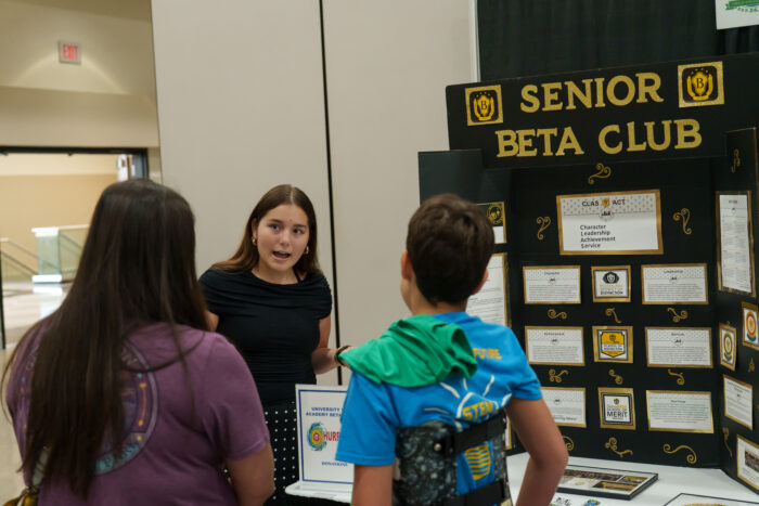 A student at the Beta Club table talks to a visiting family.