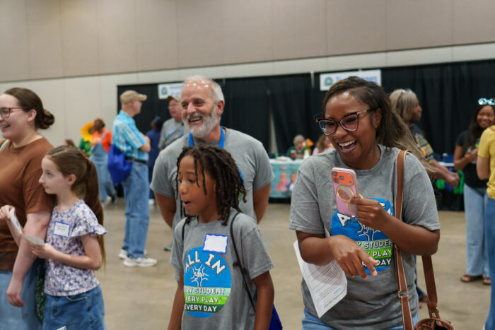 A laughing woman stands with others in front of a table at open house.