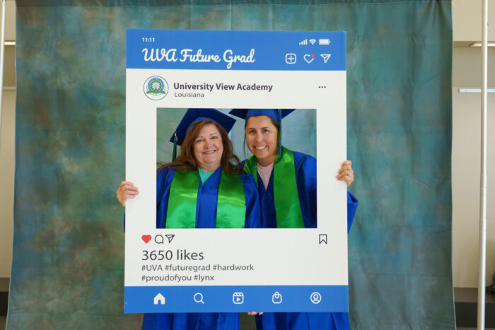 Two teachers in graduation caps and gowns pose for a picture from within a large frame that says Future UVA Grad.