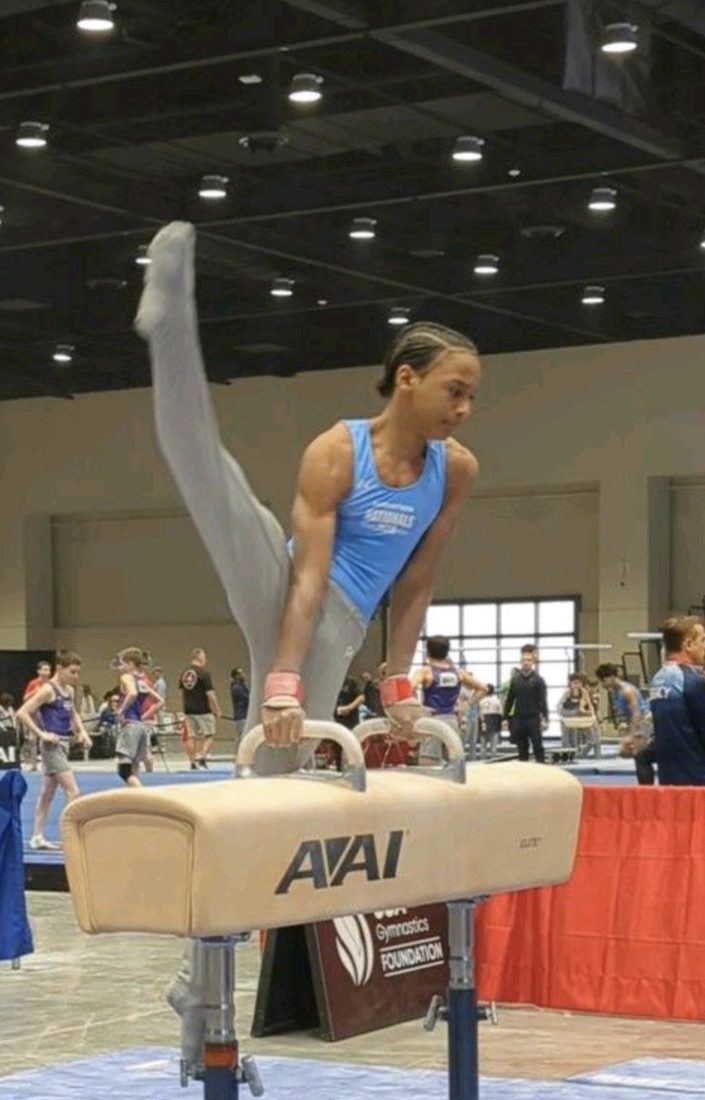 Josiah J does a scissor lift on a pommel horse inside a gym.