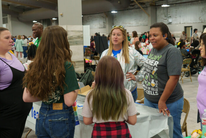 Two teachers greet a family at their table.