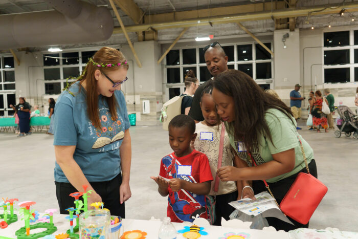 An elementary student completes an activity at a table while his family and a teacher look on.