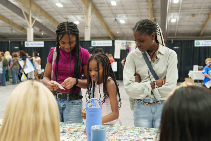 A woman and two students look at stickers on a table.
