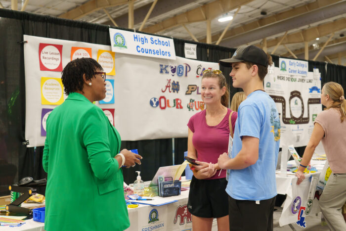 A student and his mother talk with a staff member at the high school counselors' table.
