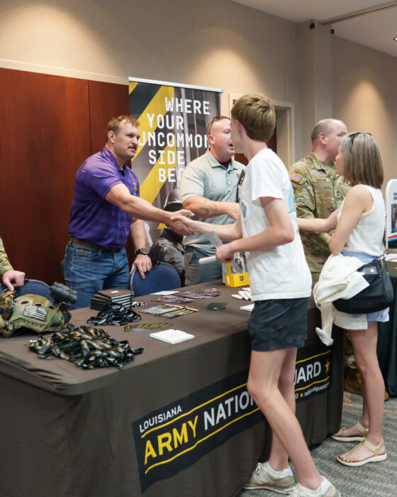 A recruiter at a Louisiana Army National Guard booth shakes hands with a student.