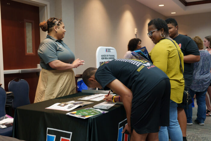 A student leans over to sign a sheet of paper at a recruiter's table.