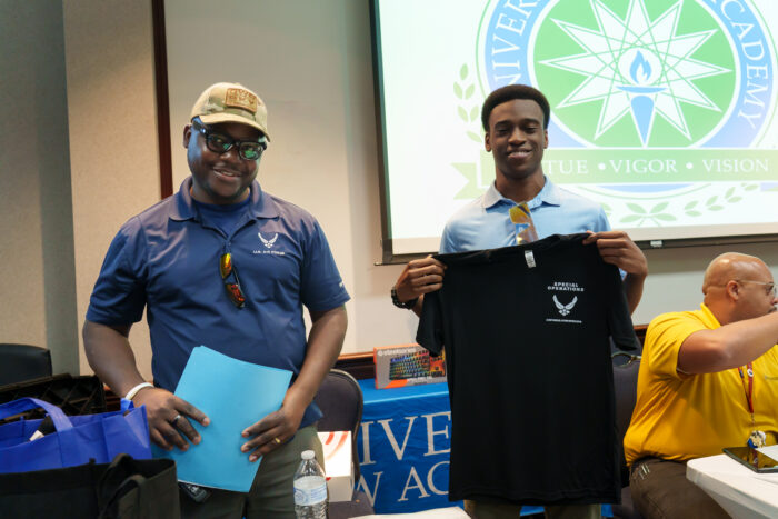 A student holds up an air force t-shirt and takes a picture with a recruiter.